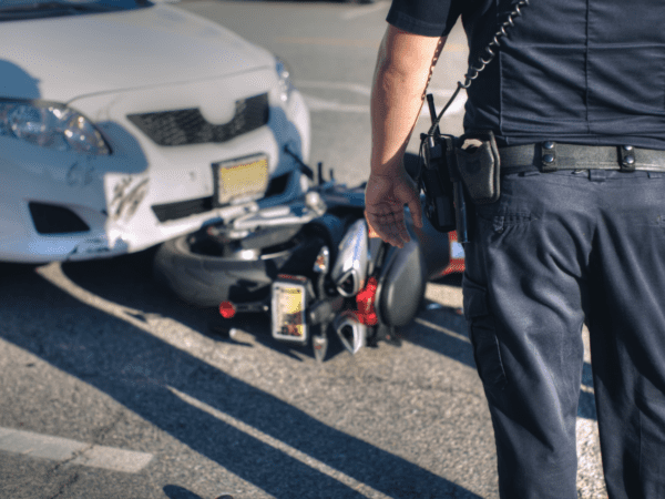 A cop is facing a crash scene between a car and a motorcycle