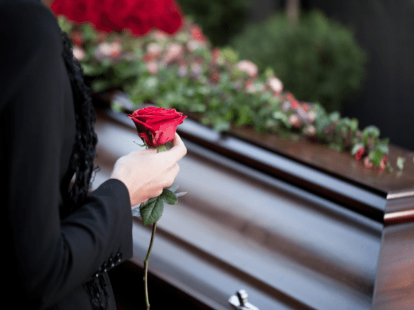 A woman holds a rose about to place it on a flower covered casket at a funeral.